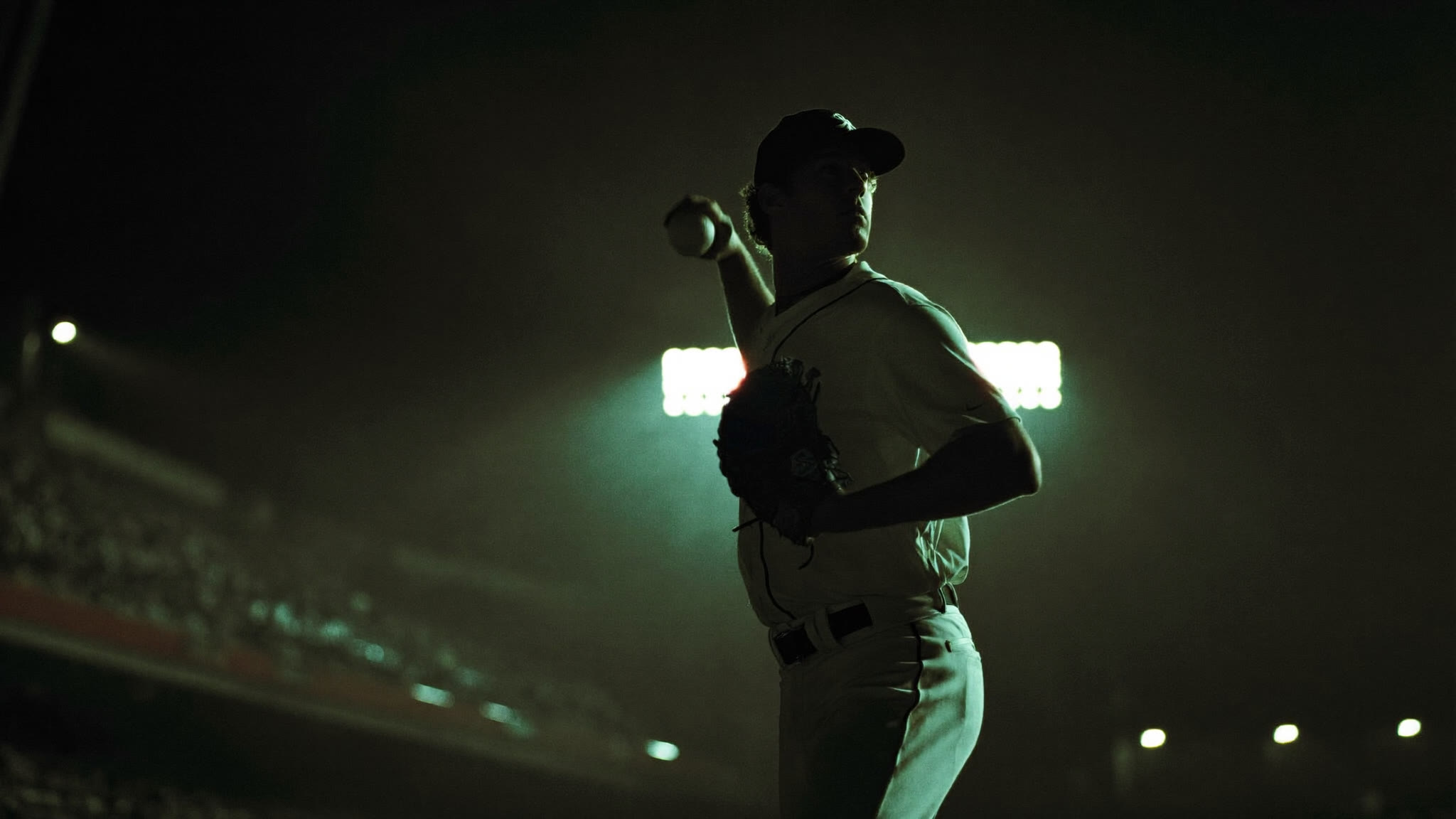 Pitcher rim-lit by stadium floodlights at night